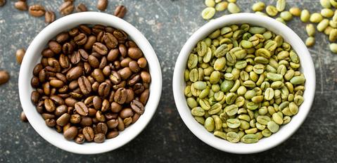 brown coffee beans in a bowl with another bowl of green coffee beans